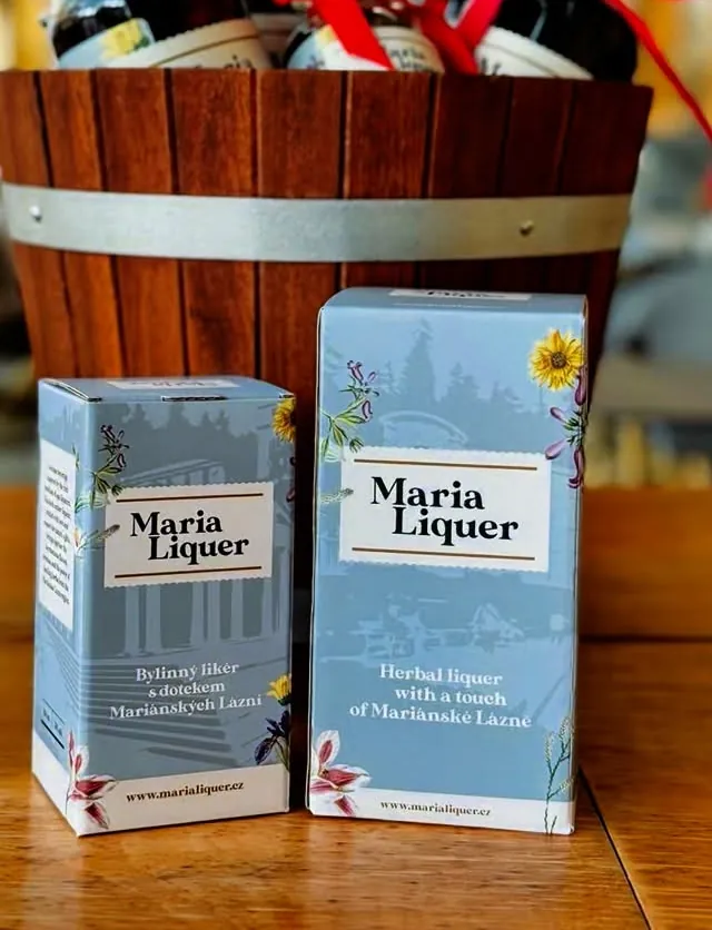 Dvě modré dárkové krabičky Maria Liquer před dřevěným sudem s lahvemi
